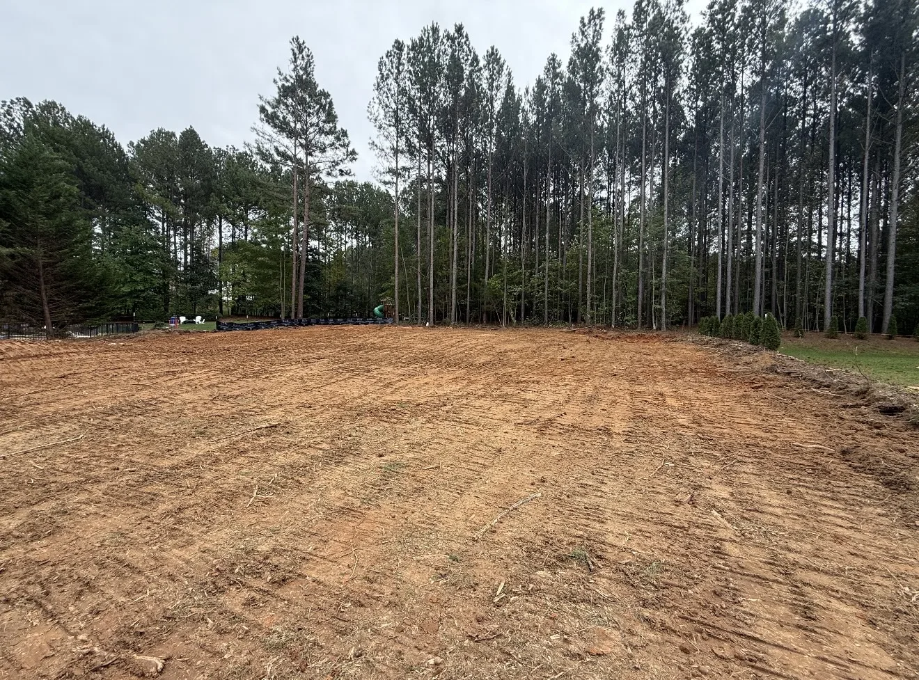 Fully cleared lot graded down to red dirt in front of a pine tree line in Mooresville, NC