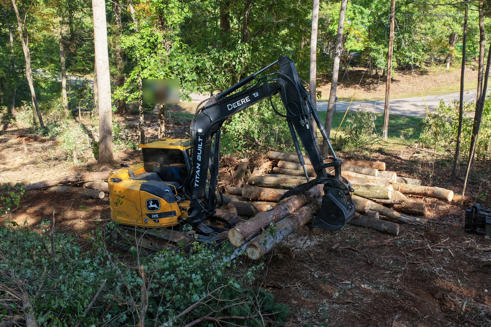 Yellow John Deere 85G excavator with TITAN BUILT on the boom stacking logs with a thumb during land clearing in Troutman, NC