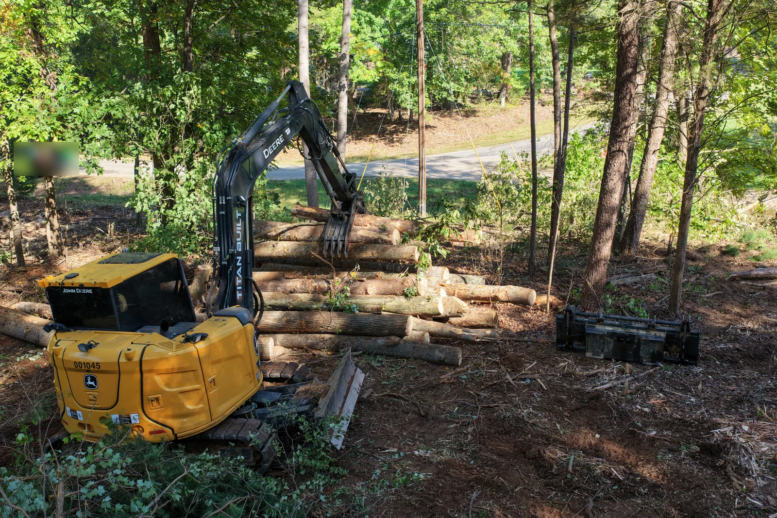 Excavator with thumb beside a stack of cleared logs on a land clearing site in Troutman, NC